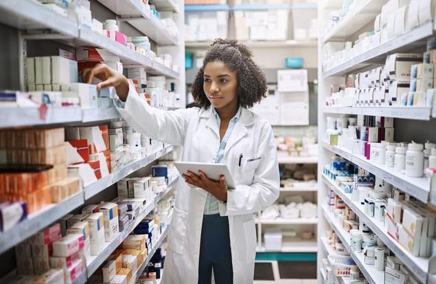 Lady pharmacist picking up medicine of the shelf with a tablet in her hand