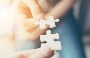 two people holding a piece of jigsaw piecing them together