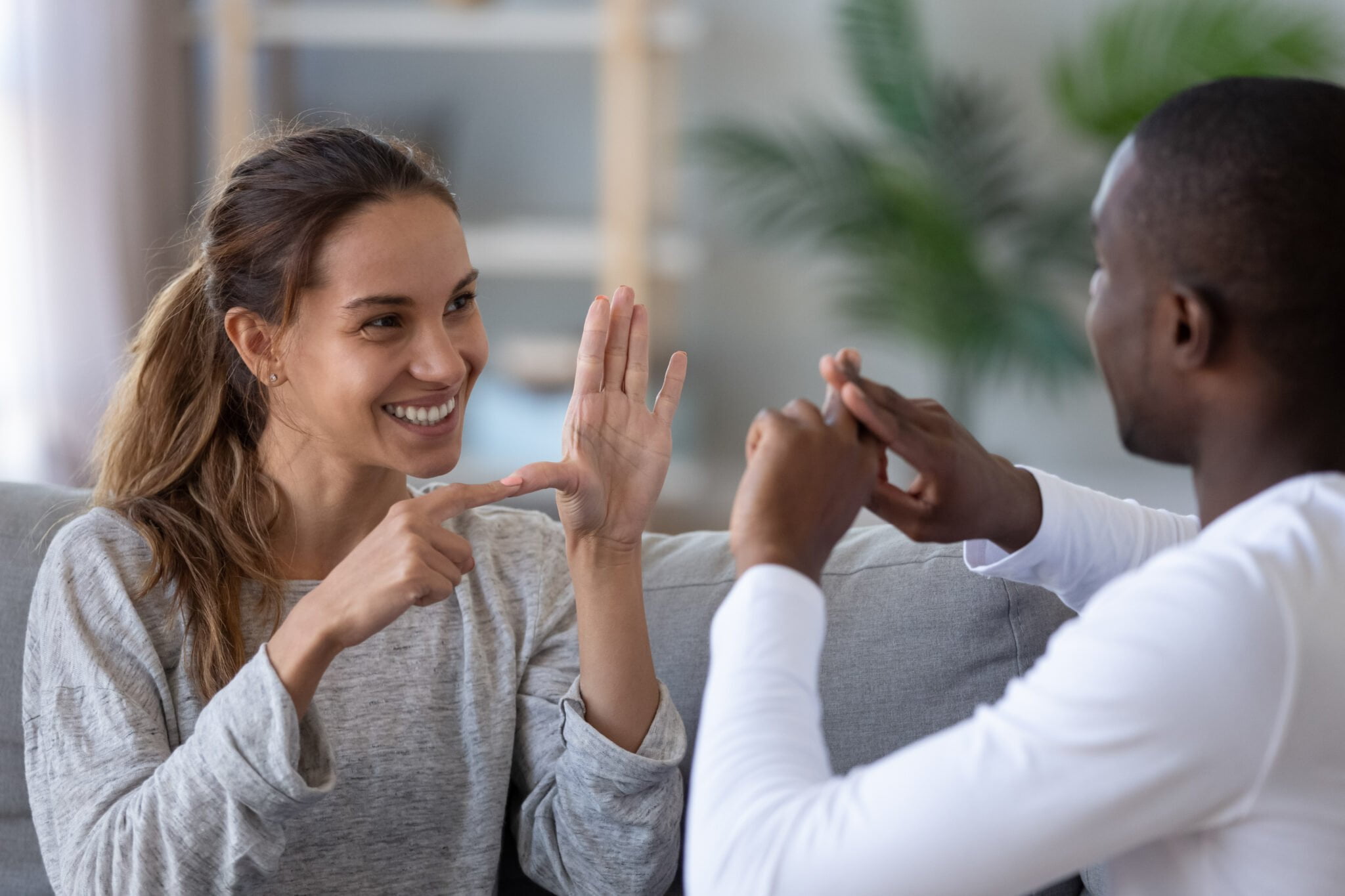 A lady sitting on the sofa doing sign language to a man