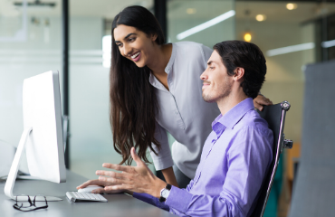 Lady standing next to a man on a computer smiling