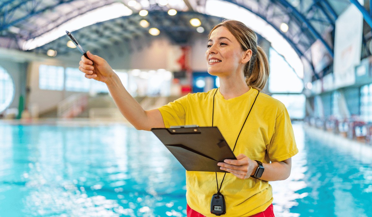 Female lifeguard holding a clipboard smiling and pointing with a pen