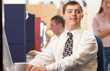 Young man in a shirt and tie working on a laptop smiling