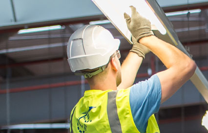 Construction worker fixing a light wearing a hard hat and a high viz jacket