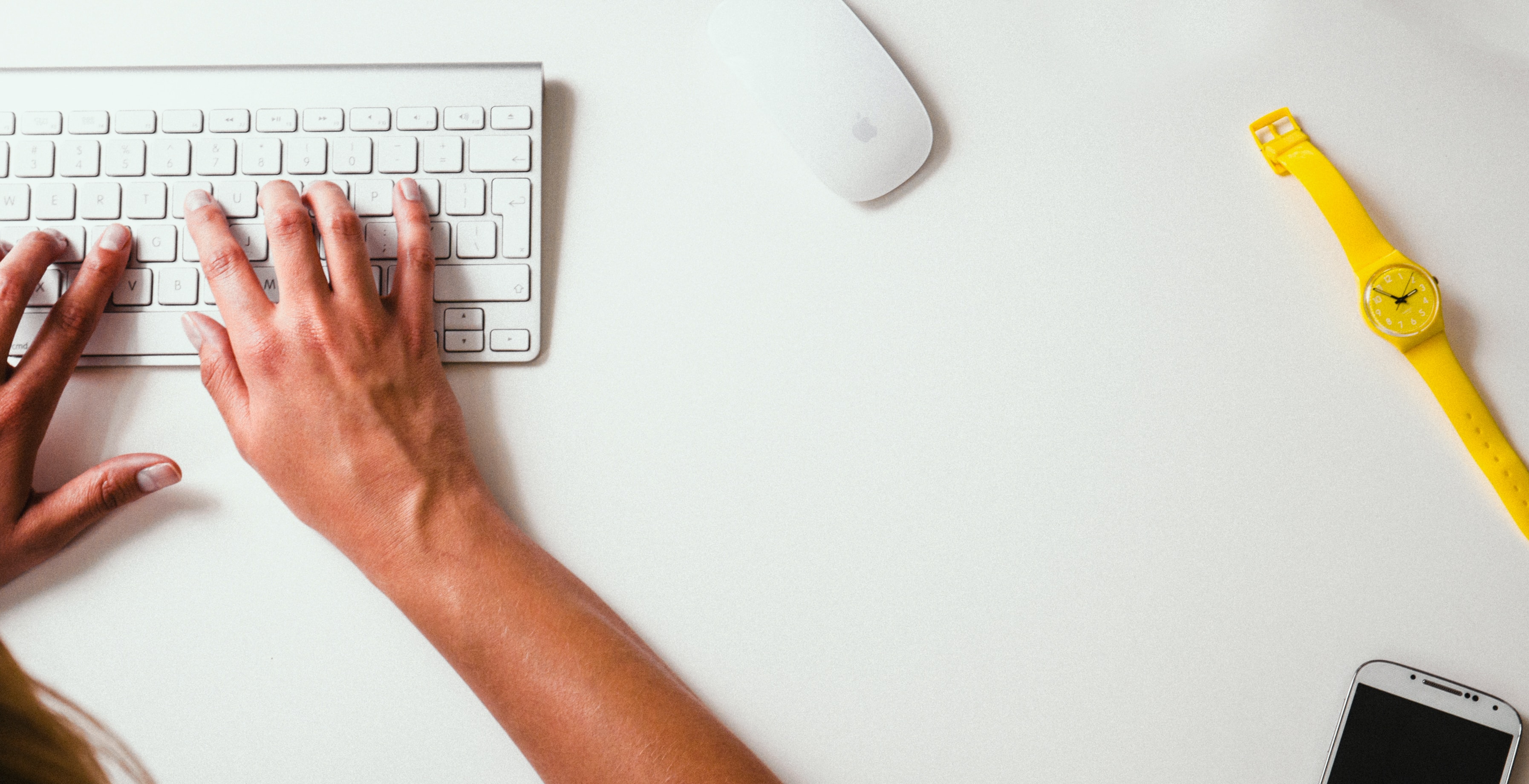 Someone typing on a keyboard with a yellow watch on the table