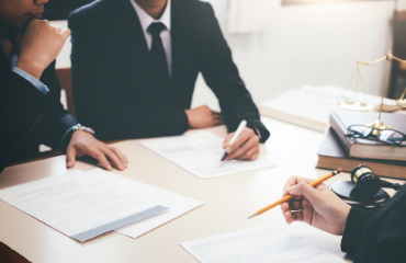 Three people sat at a desk writing on documents