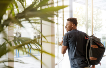 man with a backpack leaving the building through glass doors